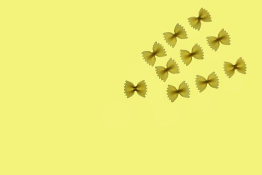 Raw pasta farfalle arranged on a yellow background ,top view ,funny composition