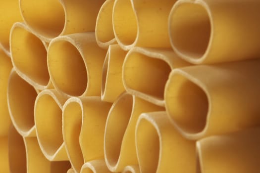 Pile of raw pasta paccheri-schiaffoni-close up traditional italian pasta ,the backlight and the diagonal angle create a graphic effect ,soft focus to give a feeling of precariousness