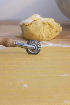  Pastry cutter wheel cuts a layer of puff pastry , in the backgroung a raw dough in the flour