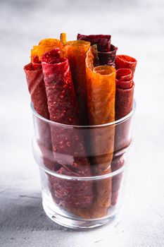 Fruit pastille in glass cup on stone concrete background. Organic sugar free roll up food made from raspberry, strawberry, peach and apple. Vegan homemade sweets. Angle view