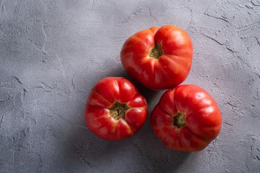 Three pink heirloom tomato vegetables, fresh red ripe tomatoes, vegan food, stone concrete background, top view