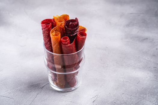 Fruit pastille in glass cup on stone concrete background. Organic sugar free roll up food made from raspberry, strawberry, peach and apple. Vegan homemade sweets. Angle view