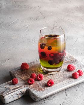 Jelly dessert with berries in glass on old wooden cutting board, sweet colorful layered pudding, stone concrete background, angle view