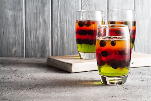 Jelly dessert with berries in glass on old wooden cutting board, sweet colorful layered pudding, stone concrete background, angle view