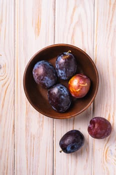 Fresh sweet plum fruits in brown wooden bowl, wood table background, top view