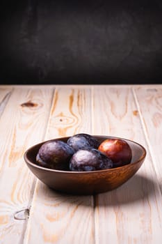 Fresh sweet plum fruits in brown wooden bowl, wood table background, angle view