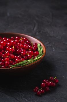 Fresh sweet red currant berries with rosemary leaves in wooden bowl, dark textured background, angle view