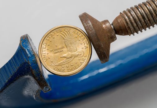 Concept for financial stress or recession. USA dollar coin being squeezed between the jaws of a large vise or vice in detailed macro shot