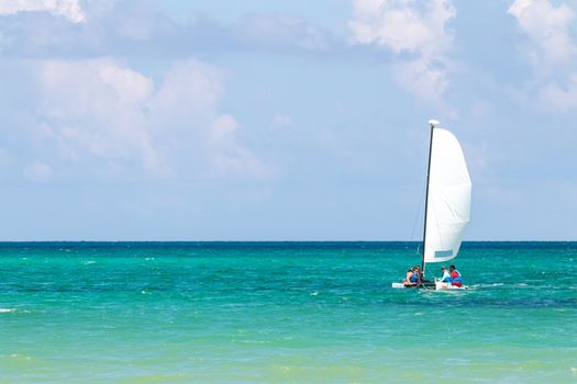 Nautical background of a white sailboat in bright sunlight, on blue ocean water, with space for text on left