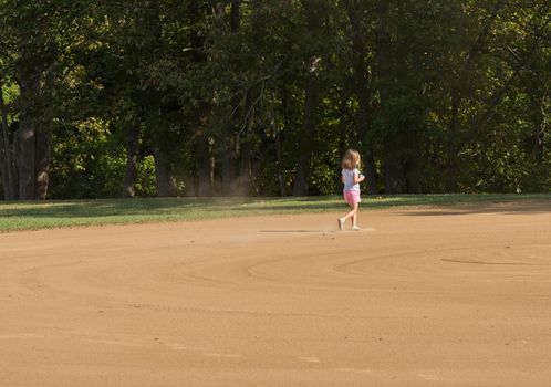 Small toddler girl playing in the sand and dirt of an empty baseball field in the infield area