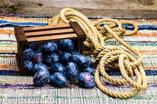 Ripe blue plums in a wooden crate in a rustic composition.