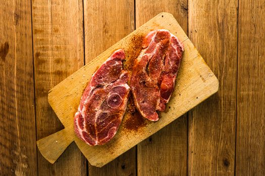 Pork chops with condiments on a wooden cutting board over wooden table, meat for bbq, top view, copy space, barbeque concept