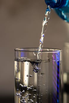 Pouring water from blue plastic bottle into a glass on blurred background. Selective focus, shallow DOF and copy space