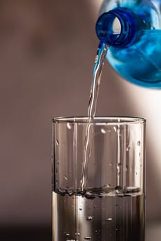 Pouring water from blue plastic bottle into a glass on blurred background. Selective focus, shallow DOF and copy space