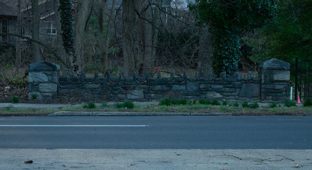 A Cobblestone Wall Across a Blacktop Street With a Dead Winter Forest Behind It