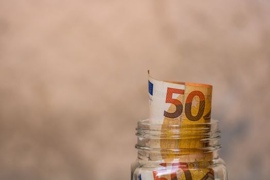 Composition with saving money banknotes (50 EURO) in a glass jar. Concept of investing and keeping money, close up isolated.