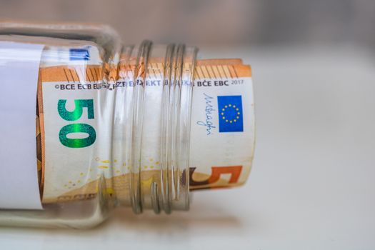 Composition with saving money banknotes (50 EURO) in a glass jar. Concept of investing and keeping money, close up isolated.