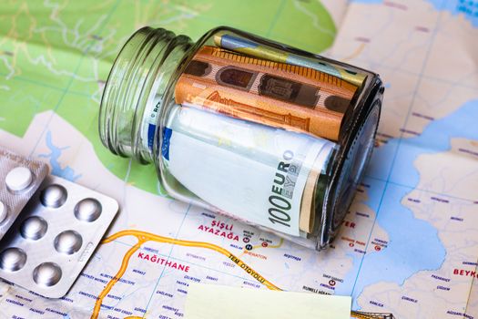 Composition with saving money banknotes in a glass jar with pills on map. Concept of investing and keeping money for healthcare and travel, close up isolated.