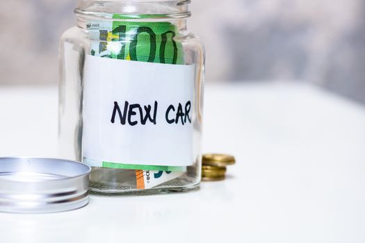 Composition with saving money banknotes in a glass jar with text new car .Concept of investing and keeping money, close up isolated.