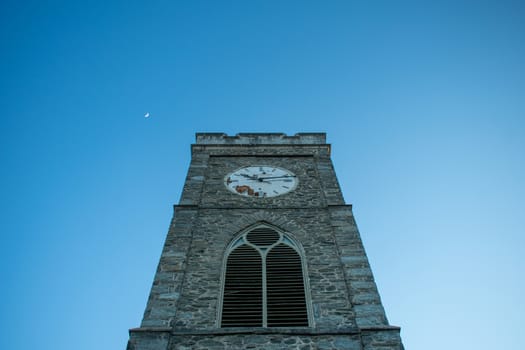 A Church's Cobblestone Clock Tower on a Clear Blue Sky