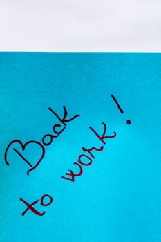 Back to work handwriting text close up isolated on blue paper with copy space. Writing text on memo post reminder