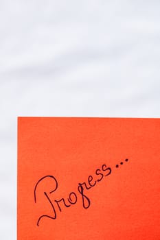 Progress handwriting text close up isolated on orange paper with copy space. Writing text on memo post reminder
