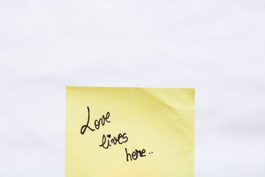 Love lives here handwriting text close up isolated on yellow paper with copy space.