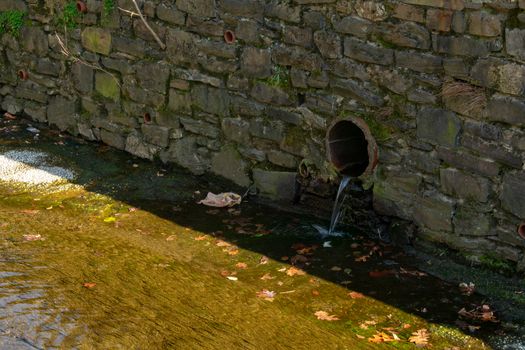 A Drainage Pipe in a Cobblestone Wall Pouring Into a Man-Made Stream