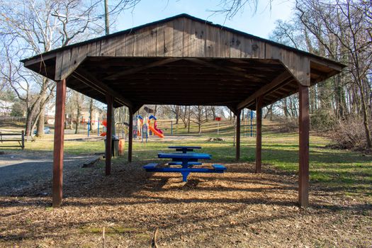 A Large Wooden Gazebo in a Park in the suburbs With Picnic Tables Underneath