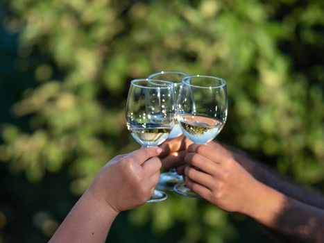 White wine glasses in hands. Two unrecognizable people clang glasses together outdoors.