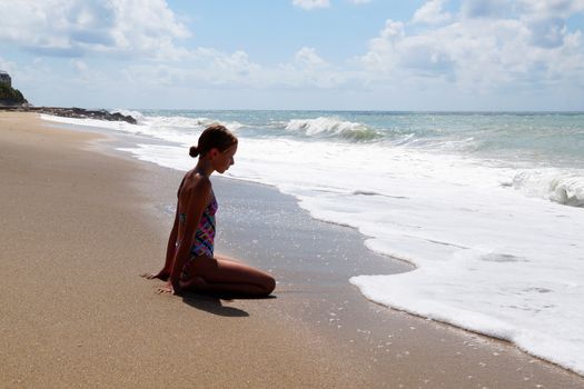 teenage girl sitting on the sand by the sea.