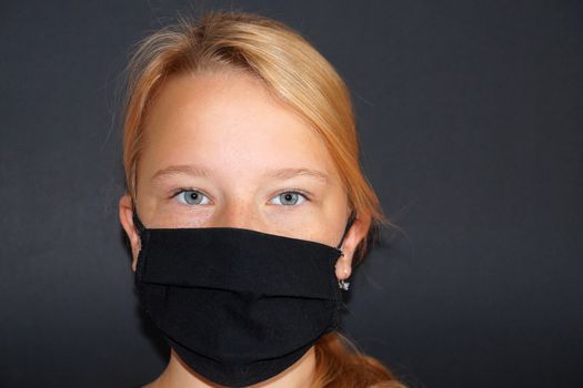 teenage girl in a black medical mask on a black background, portrait