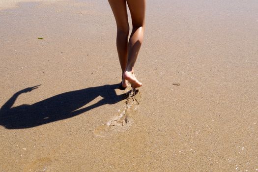 child feet walk on wet sea sand, back view.