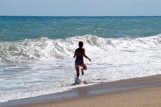 teenage girl happily runs along the sandy seashore next to the big waves.