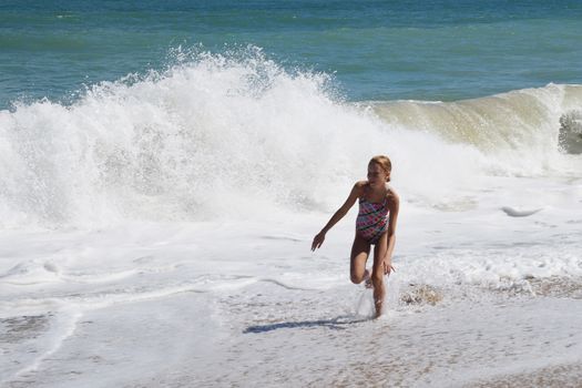 teenage girl happily runs along the sandy seashore next to the big waves.