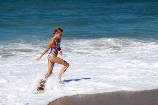 teenage girl happily runs along the sandy seashore next to the big waves.