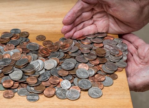 Hundreds of US coins being gathered into hands on wooden table as concept for hoarding during shortage of loose change