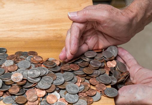 Hundreds of US coins being gathered into hands on wooden table as concept for hoarding during shortage of loose change