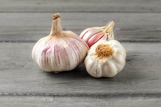 Garlic bulbs, purple cloves under cracked skin on gray wood table.