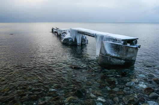 Wooden pier in sea covered with ice and snow with icicles.