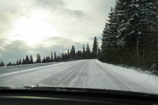 View from driver's seat on road covered with snow, strong blinding sun back light, risky driving conditions.