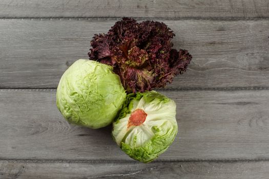 Top view on iceberg salad and Lollo Rosso (red coral leaf lettuce) on gray wood desk.