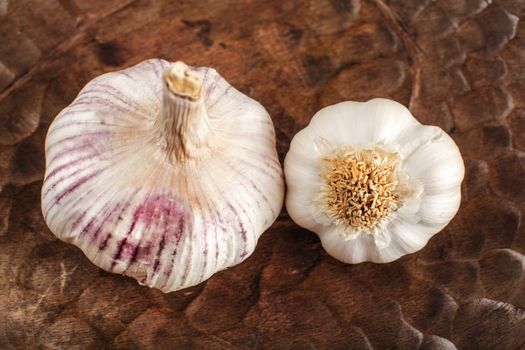 Top view on garlic bulbs, cloves covered in purple skin with crack, in old wooden bowl.