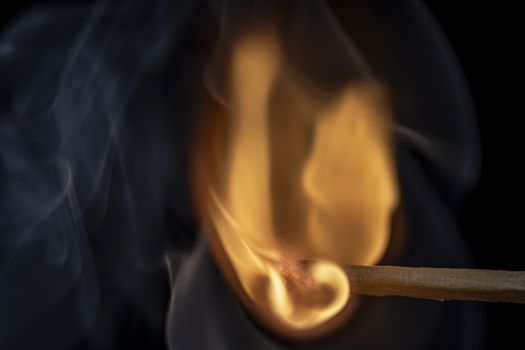 Match burning with smoke after being lit showing flame against  black background.