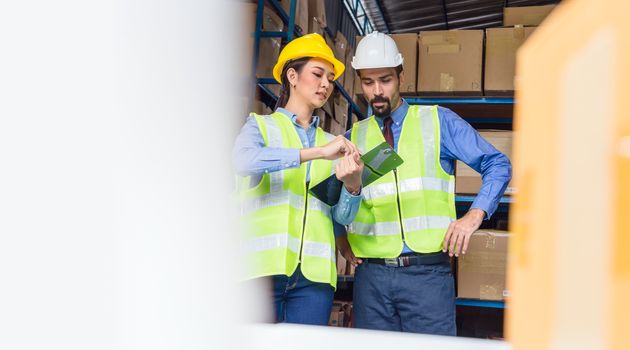 Manager of warehouse worker assign and command in serious look to assistant manager woman in local warehouse or factory, Asian and white caucasian people,Partner and colleague working together concept