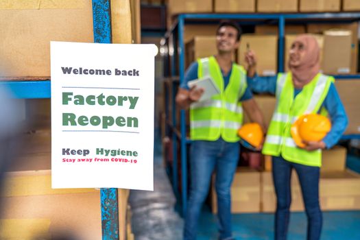 Closeup factory reopen notice paper tag for welcome back to customer into local warehouse after Covid-19 is gone over the Muslim woman and Indian man worker working together background,