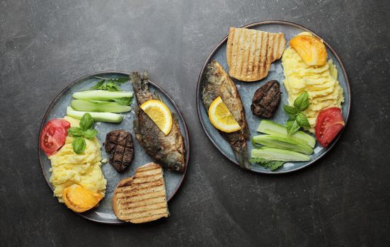 Fried fish, meat steak and vegetables on a plate. Concrete gray countertop. High quality photo