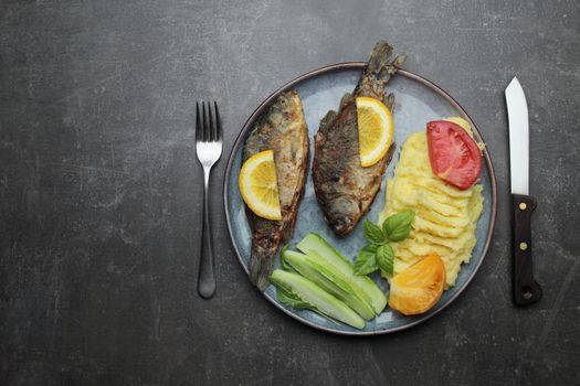 Fried fish and vegetables on a plate. Concrete gray countertop. High quality photo