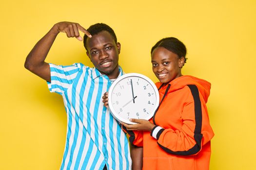 Young couple of african appearance holding a watch in yellow hands isolated background dating family