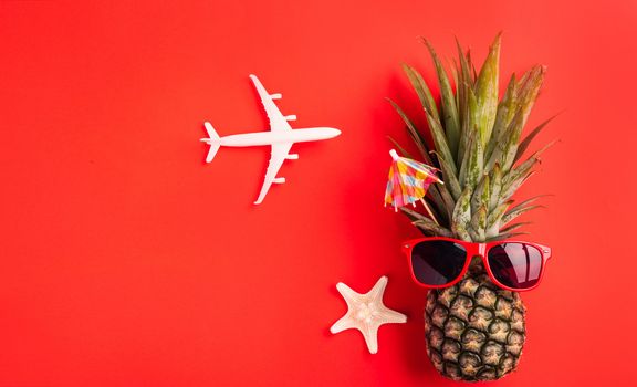 Celebrate Summer Pineapple Day Concept, Top view flat lay of funny fresh pineapple wear red sunglasses with model plane and starfish, isolated on red background, Holiday summertime in tropical